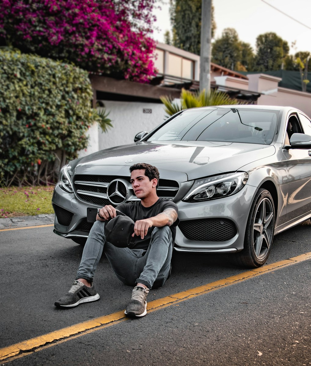 unknown celebrity sitting siting beside silver Mercedes-Benz car outdoors with auto policy